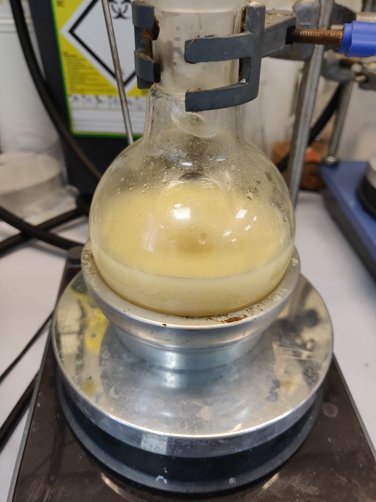 A round bottom flask on a stirrer plate with a pale yellow suspension stirring in it
