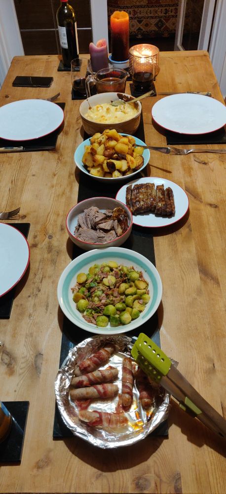 The Christmas dinner table ready for serving, with pigs in blankets, sprouts and bacon, carved roast lamb, sliced stuffing, roasted potatoes and parsnips, cauliflower cheese and gravy