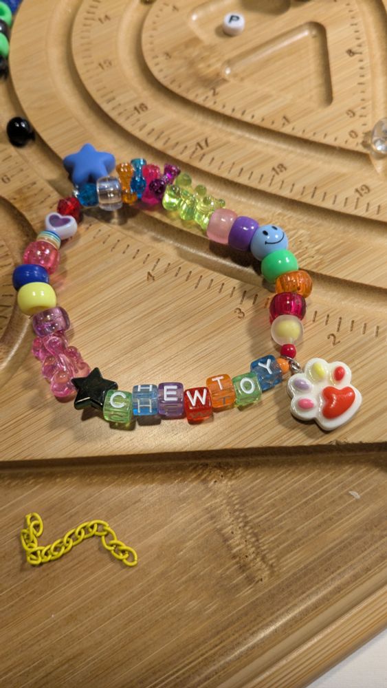 a kandi bracelet. it's got rainbow beads and says "chewtoy" 