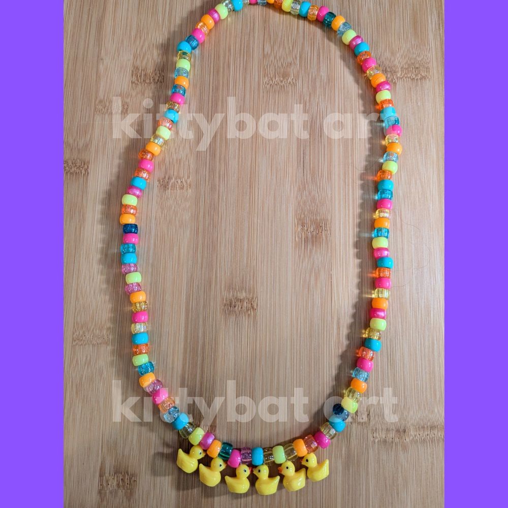 a necklace made of pony beads. the beads are orange, blue, hot pink, and yellow. there are 6 rubber ducky charms at the bottom of the necklace