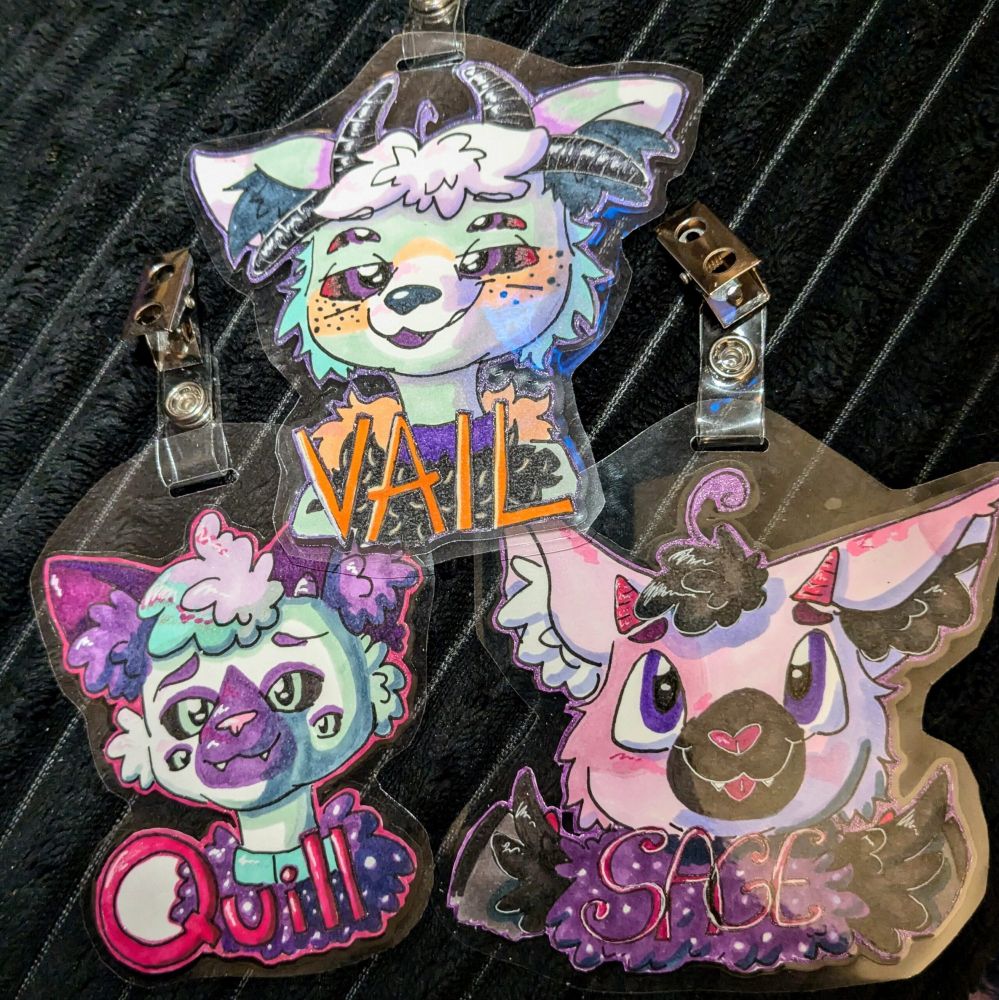 three laminated furry headshot badges. they say Vail, Quill, and Sage