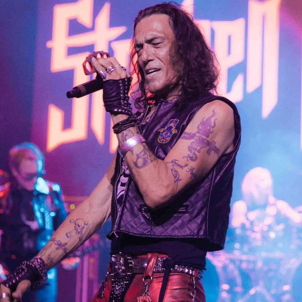 Stephen Pearcy, singer of Ratt. It’s a recent photo and he’s on stage singing into a mike. He’s dressed in classic hair metal regalia. 