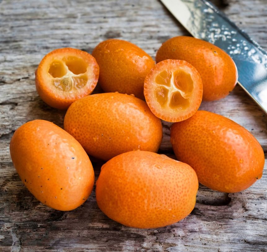 kumquats - small oval orange citrus fruits - including one cut in half, on wooden board