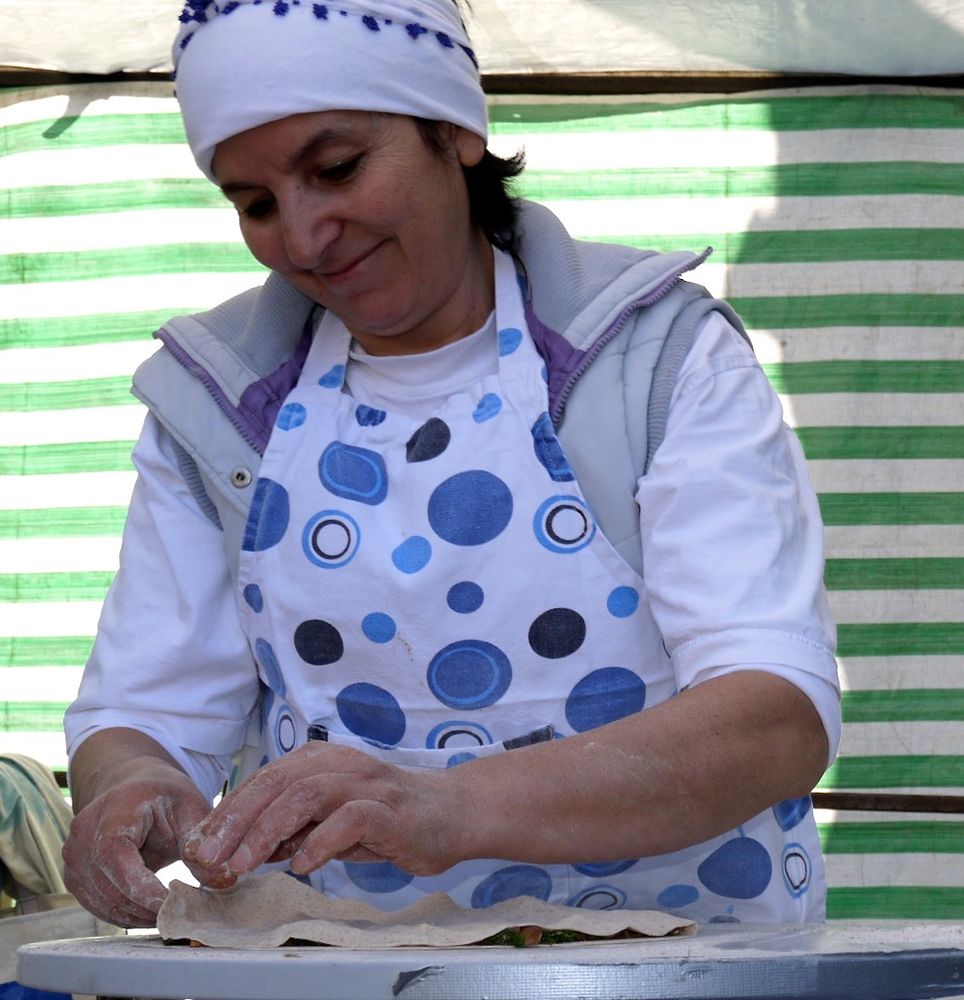 Smiling woman in headscarf and blue spotty apron making gozelme - Turkish pancakes - on market stall