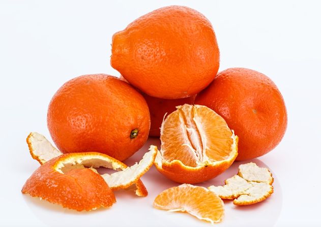 pile of five citrus fruits with reddish skin, one opened to reveal thin skin and tangerine-like segments