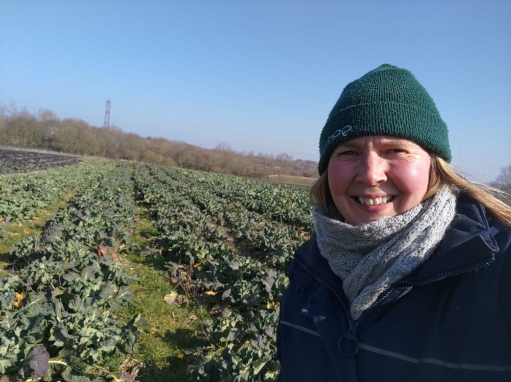 Woman in hat and scarf with field of crops and blue sky in background
