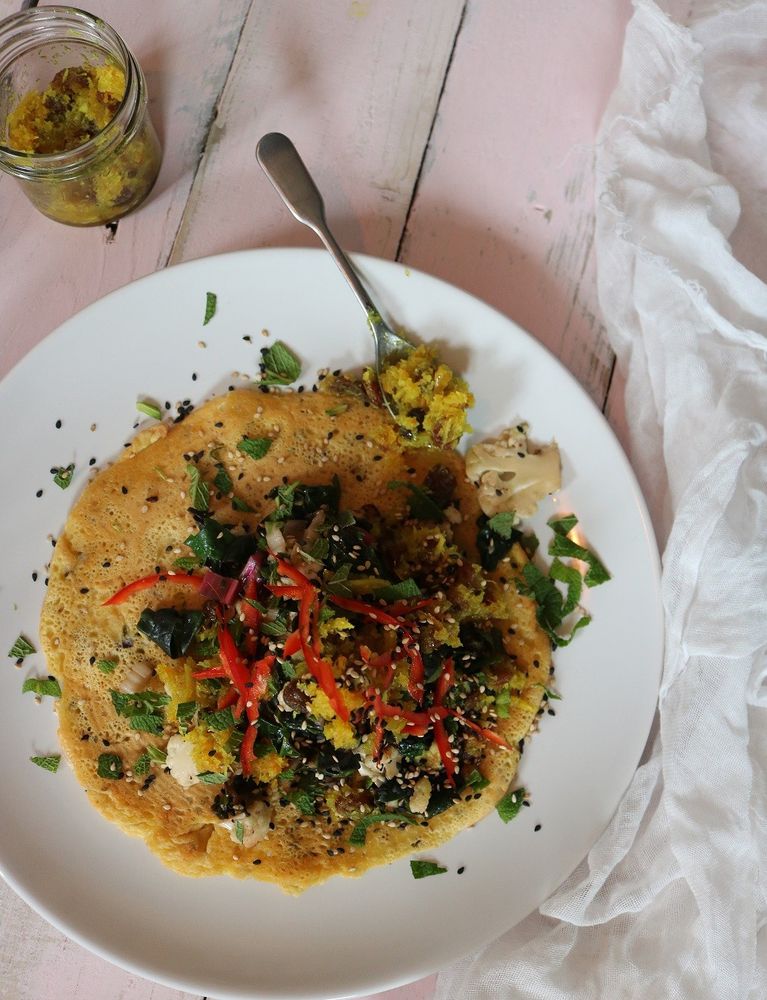 savoury socca pancake on white plate with vegetables on top and pot of chutney