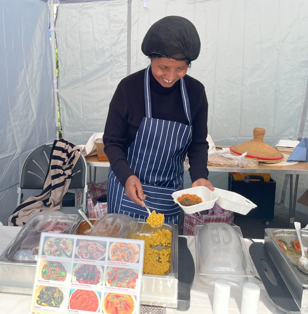 Chef Tekuam at Ethiopian food market stall spooning yellow lentils into box with other mixed vegetables