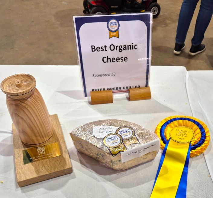 Table showing large piece of blue cheese, trophy, rosette and sign saying "Best Organic Cheese"