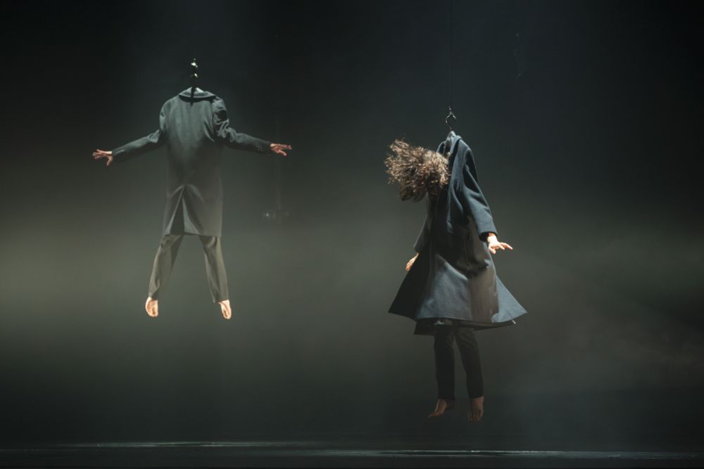 Des gens sont soulevés par leur trop grand manteau accroché à un cintre, tiré vers le plafond par un câble.