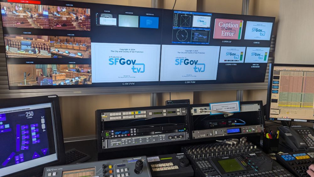 This is an image of the inside of one of SFGovTV's control rooms, where all our live broadcasts are transmitted. In this picture, several monitors display six different camera shots of a commission room, preview and on-air monitors with the SFGovTV legal copyright and logo, and various other smaller screens with other visual aids for live broadcasts. Also in the picture is an audio mixer, a camera switcher, a remote camera control board, decks to record the meetings, a phone, a computer and keyboard.