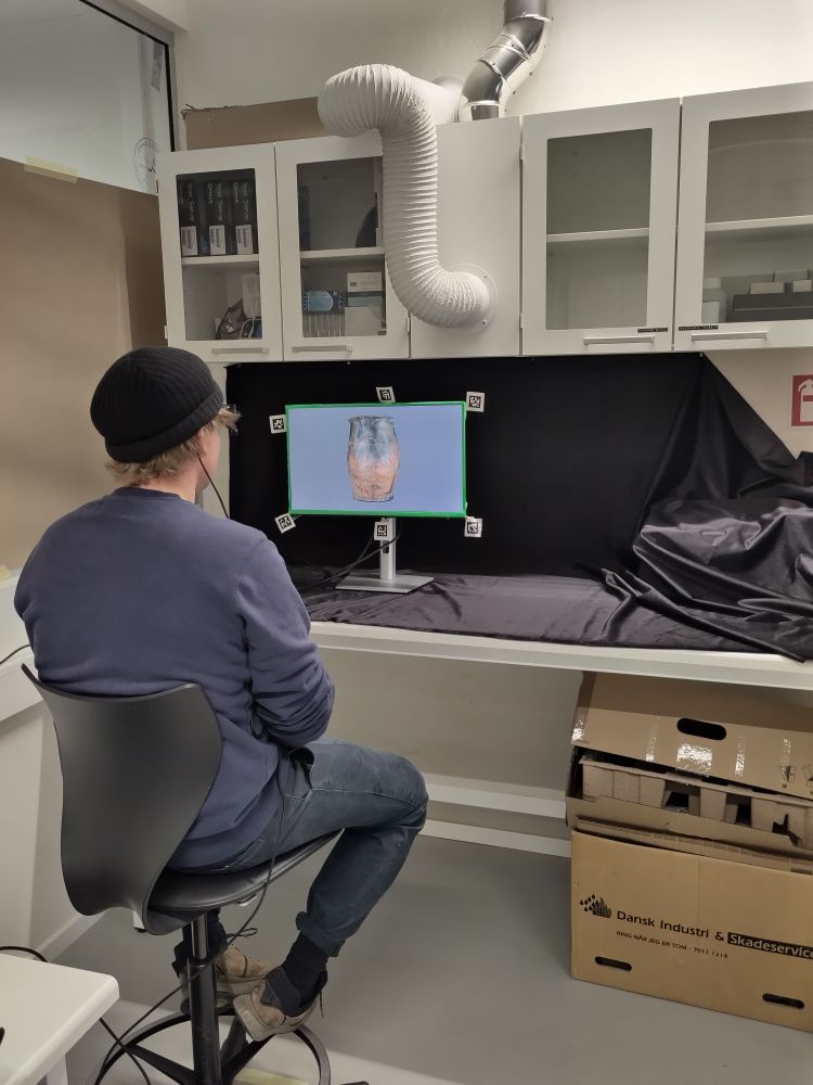 A man looking at a monitor where pictures of ceramics are displayed.