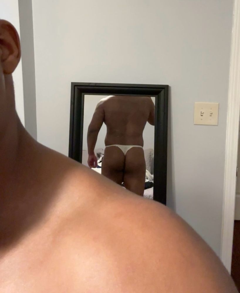 male figure with thong on in mirror taking a selfie with his back and butt showing 