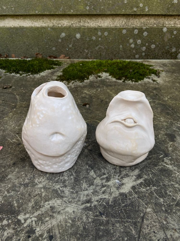 Two white pots, one has a belly and one has an eye