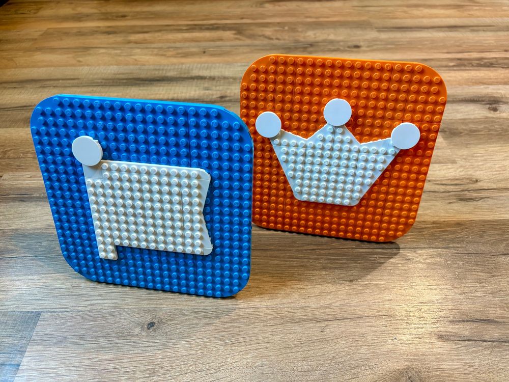 Two icons built with LEGO bricks. A white flag on a blue square base for the Font Awesome logo, and a white crown on an orange square base for the Web Awesome logo.