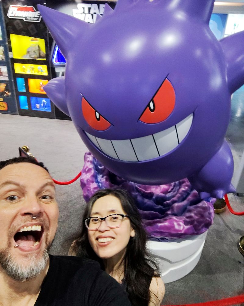 Photo of two smiling people in front of a Pokemon Gengar statue.