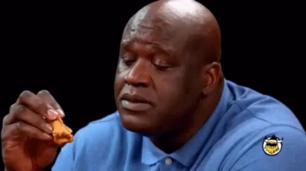 a bald man in a blue shirt is eating a piece of fried chicken