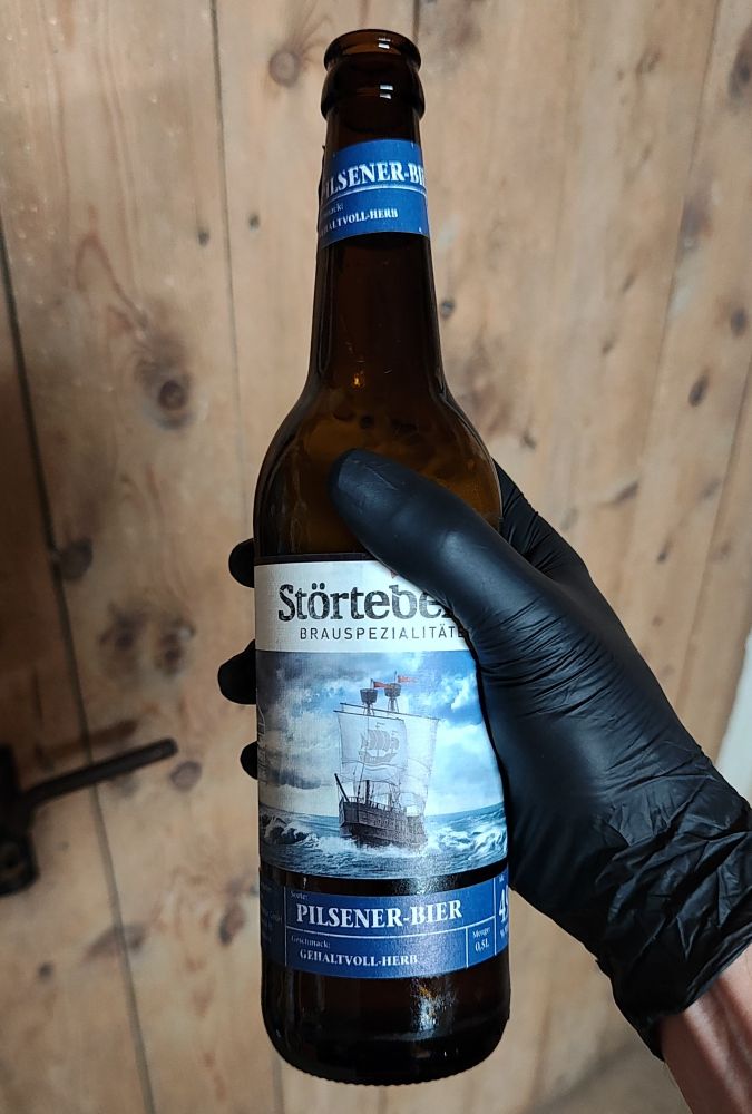 Flasche Bier in Hand mit schwarzem Latexhandschuh. Im Hintergrund eine alte Holztür.