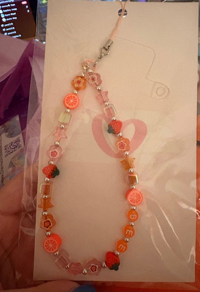 beaded wristlet charm for a phone with different orange and pink colored beads, orange and strawberry slice beads & orange beads that spell out my name “bee”