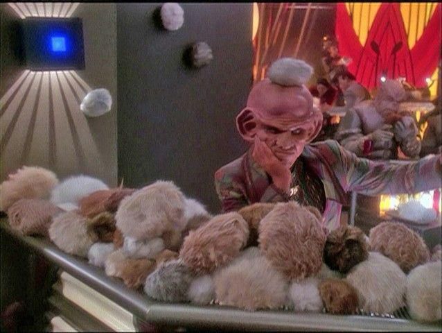 Screencap of Star Trek: Deep Space 9, wherein a crestfallen Quark looks out over the masses of tribbles which have overrun his bar. One is balanced on his head.