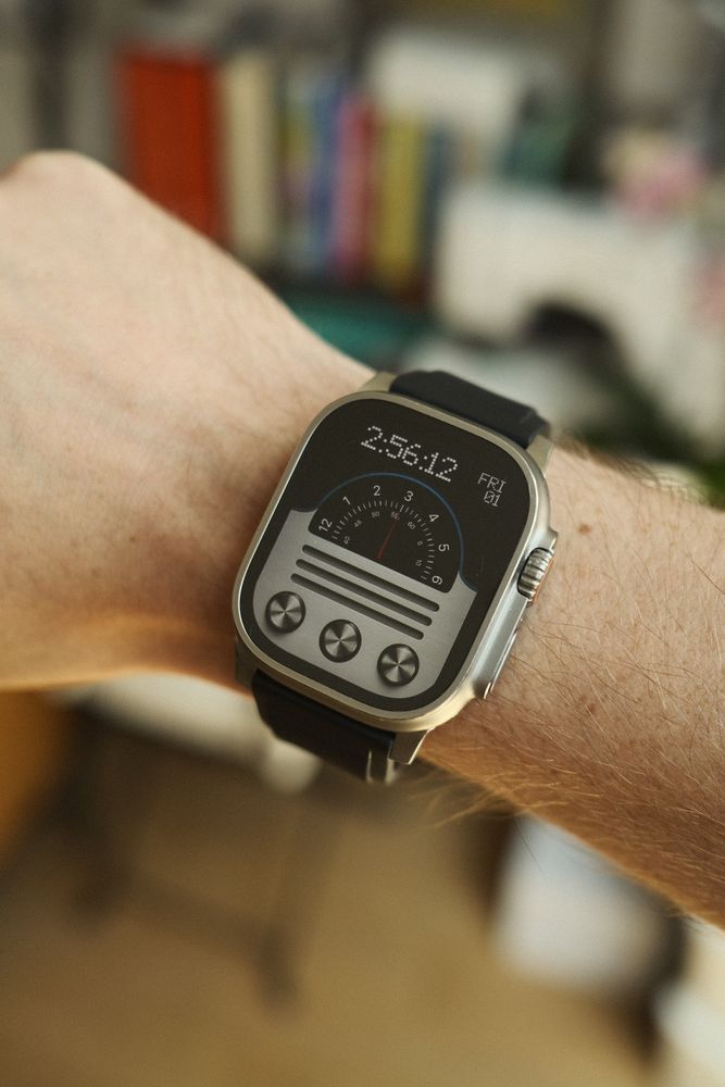 A close-up image of a person's wrist wearing a modern smartwatch with a rectangular face and a black strap. The watch face design features a unique retro-inspired graphic resembling an old radio dial with a needle indicator and three round knobs at the bottom. The background is softly blurred, highlighting the watch and wrist in sharp focus.