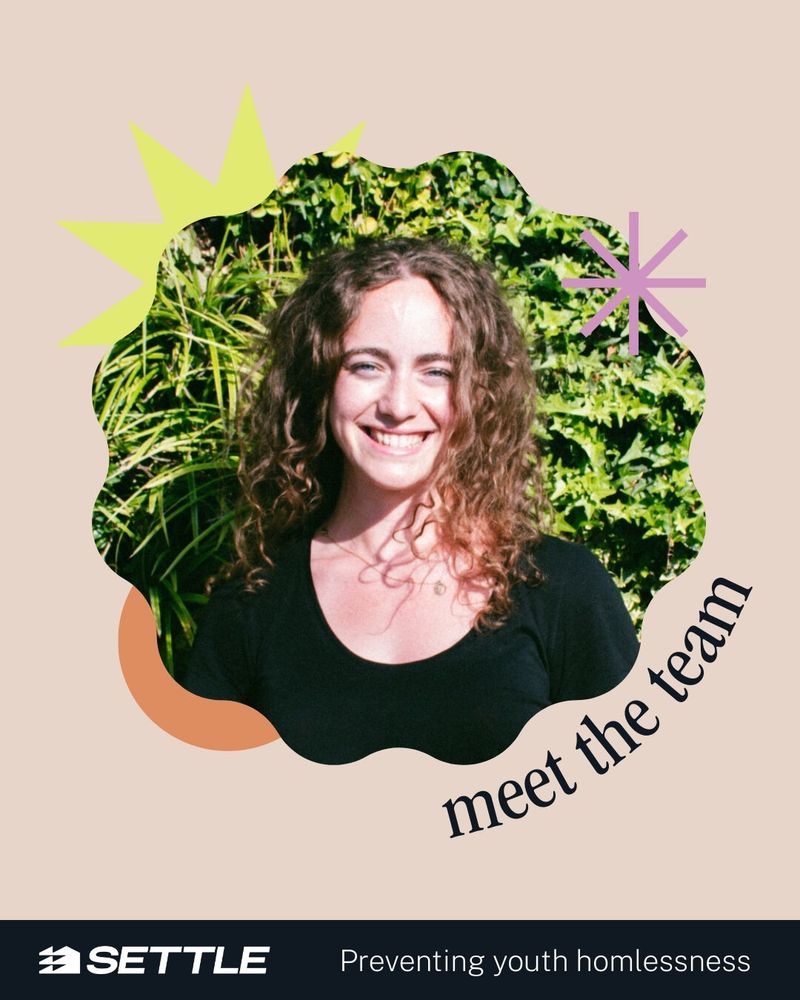 A photo of Alice smiles to camera standing infront of a floral background