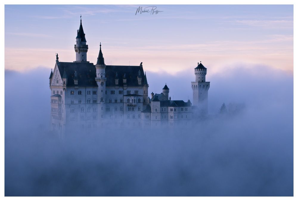 Ein schönes Schloss mit mehreren Türmen eingehüllt in Nebel,so dass nur das Schloss sichtbar ist.Darüber ein kaum bewölkter Himmel in der Abenddämmerung