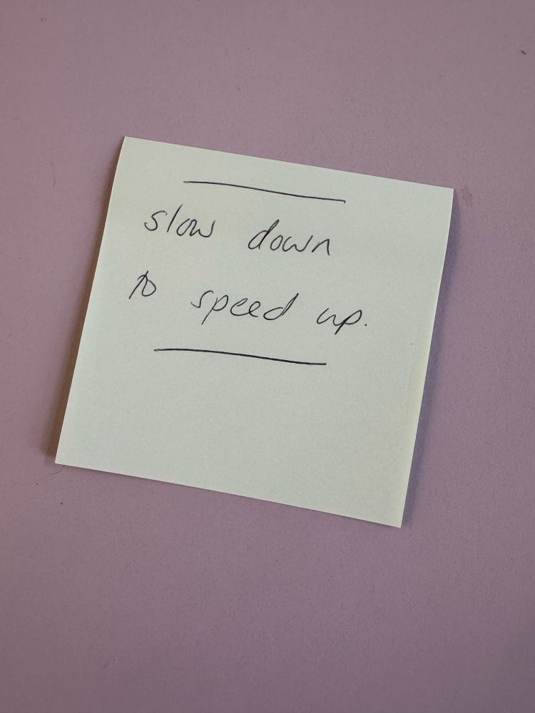 A yellow post it with ‘slow down to speed up’ handwritten on it