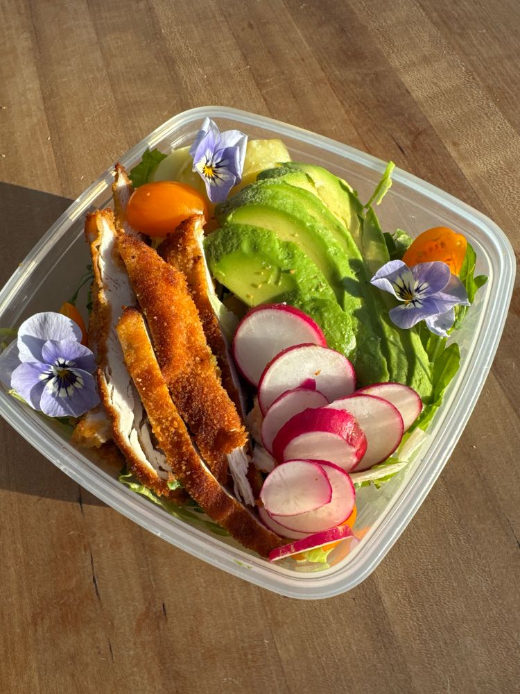 A colourful and delicious looking salad lunchbox, with breaded chicken, avocado and edible flowers