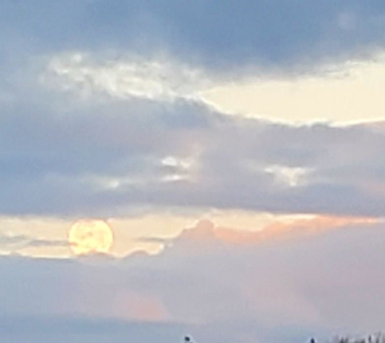 Full moon in lower left corner surrounded by pink tinged clouds