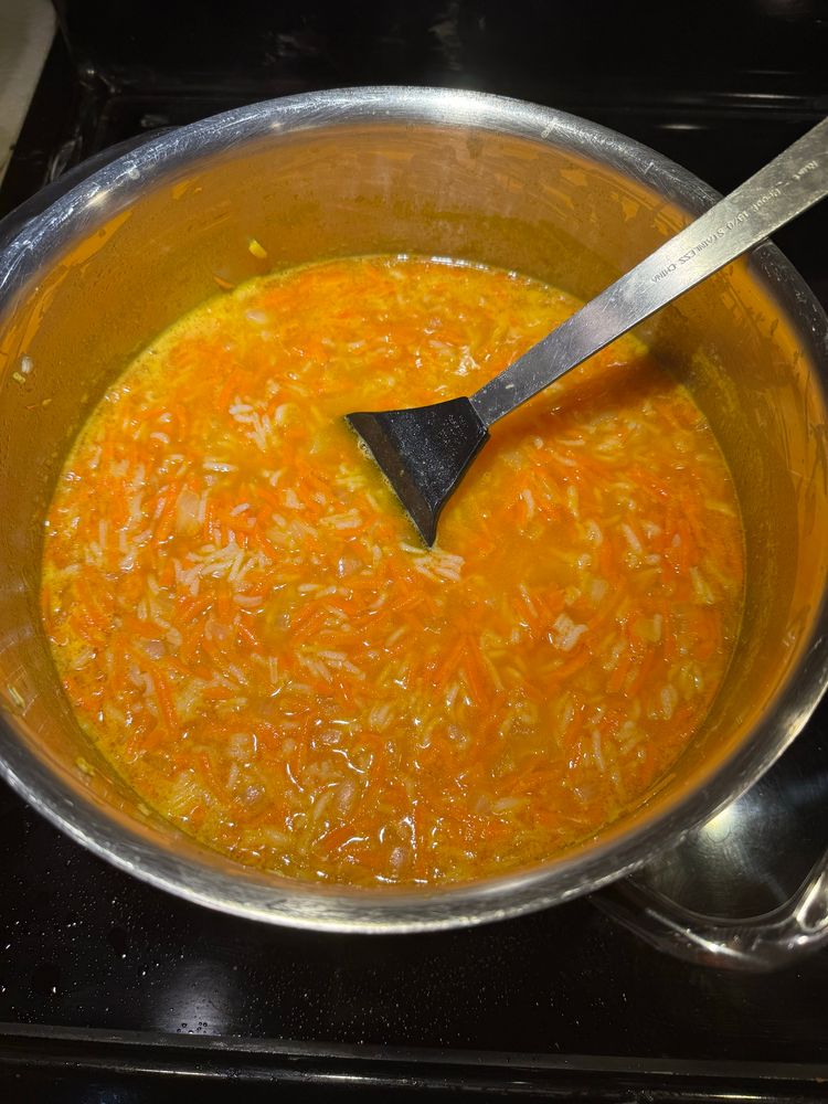 A pot full of carrot soup. It’s a beautiful orange color, you can see shredded carrots and rice. 