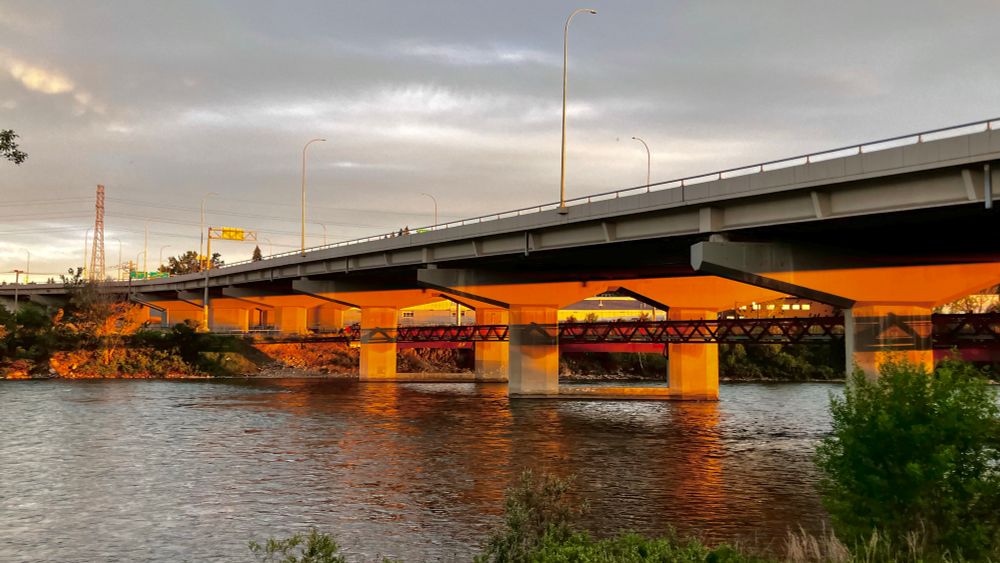 The underside of the Crowchild Bridge in Calgary, taken from the north bank of the Bow River just before sunset. The setting sun's rays cast a warm glow on the struts. Also visible is the pedestrian and bicycle crossing.