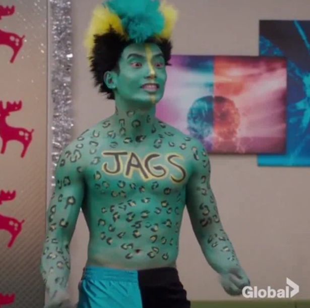 A man painted teal with jaguar spots with a teal and yellow wig and "JAGS" painted across his chest in black with gold outline wearing teal and black pants. From the TV show "The Good Place"