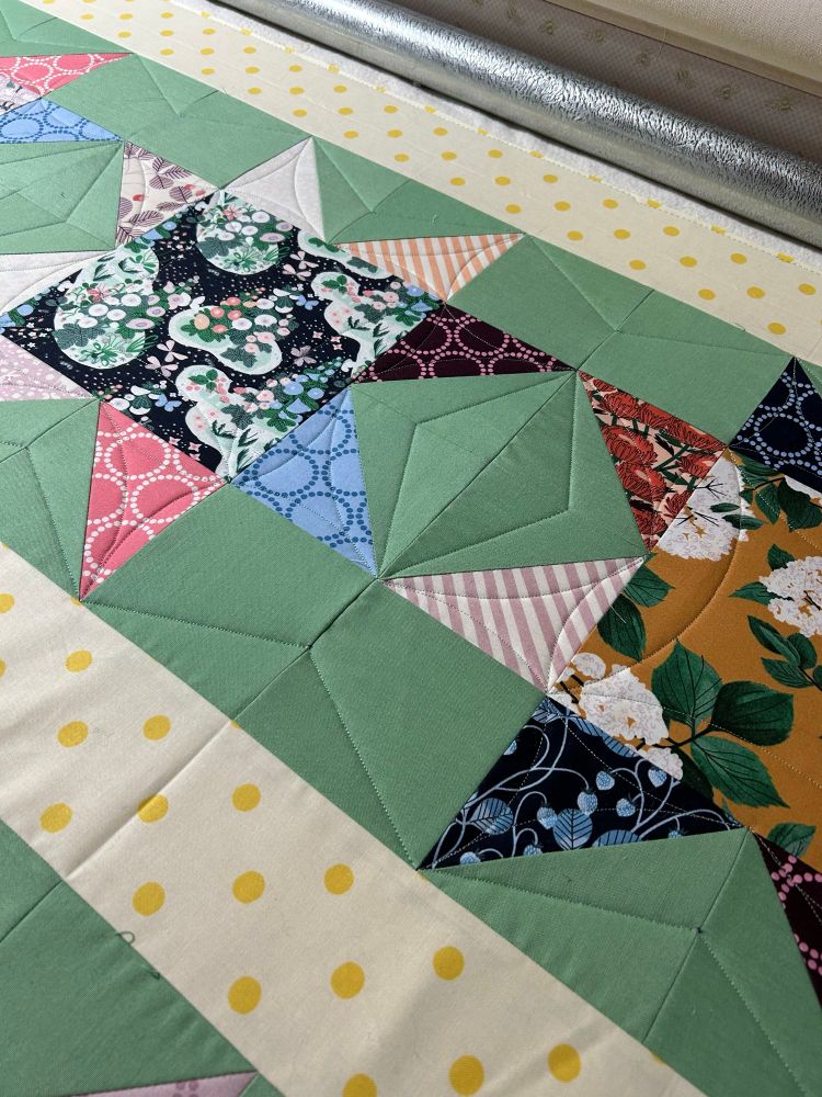 Pieced floral fabric stars, on mint green background, with angular ruler quilting lines