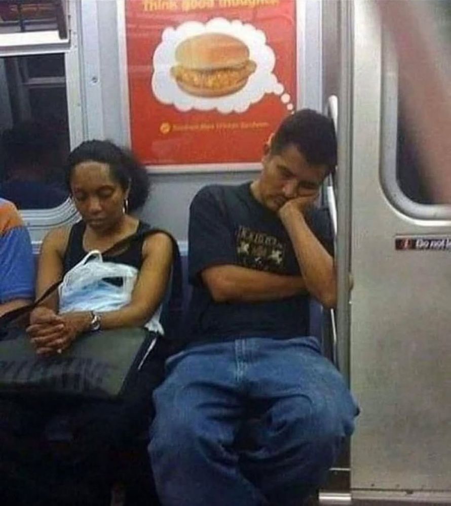 guy sleeping on metro train sleeping while sitting, where it looks like the advertisement behind him is displaying him thinking about a chicken sandwich 