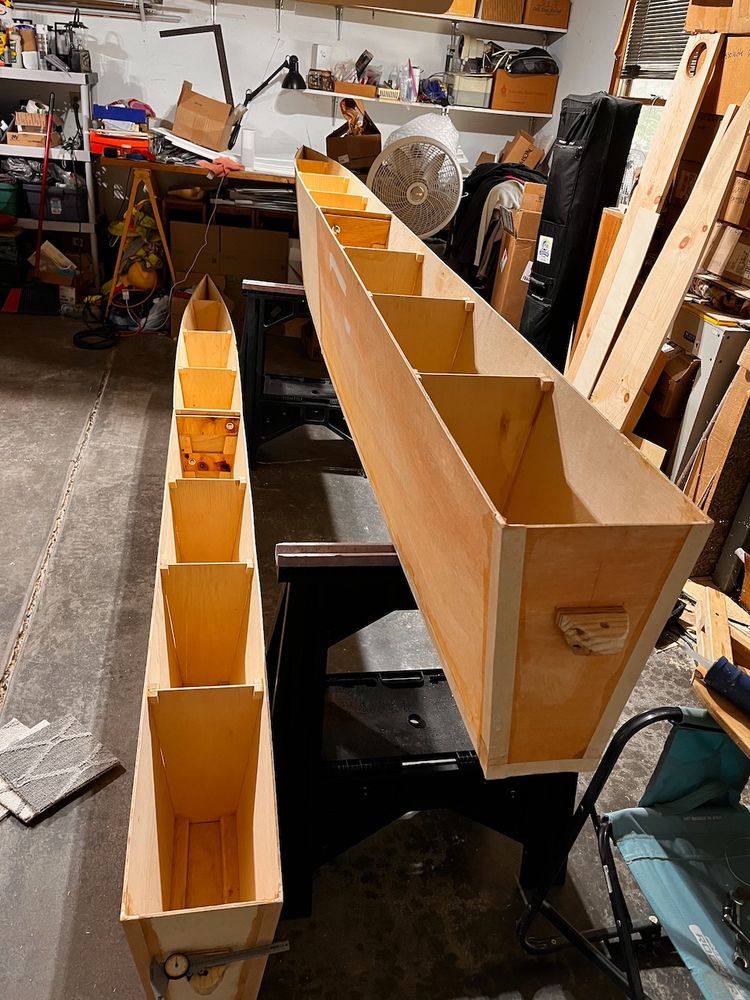 Two partially built catamaran hulls viewed from the top and back. They have plywood sides, and plywood supports throughout.