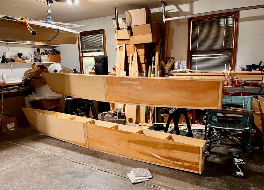 Two partially built catamaran hulls viewed from the side, sitting in a garage.