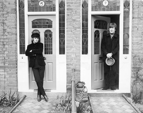 Black and white photo of Ringo Starr and John Lennon of The Beatles standing in the doorways of two adjoining houses.