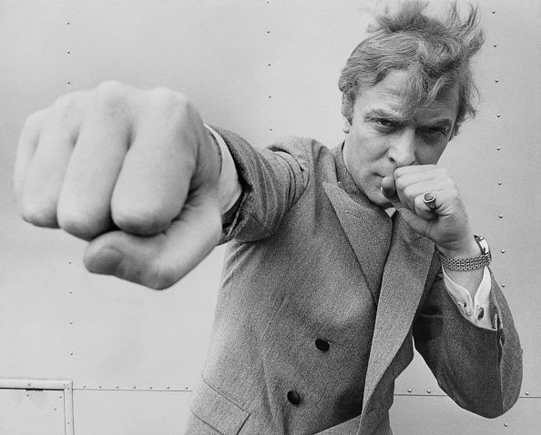 Black and white photo of Michael Caine throwing a punch, taken August 1965.