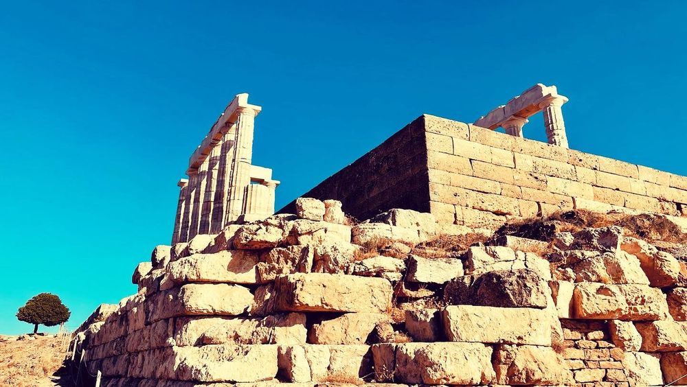 Ancient Greek ruins with weathered stone foundations and columns standing tall against a bright blue sky