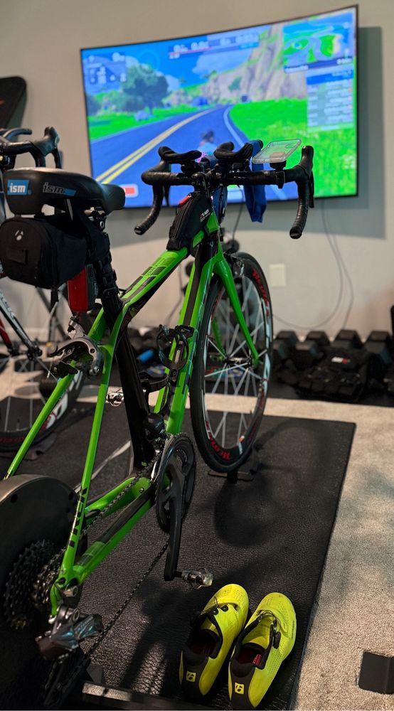 Lime green Trek road bike on a smart trainer and black mat in front of a TV with Zwift displayed.