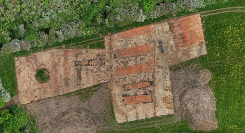 An aerial view of 8 rectangular 'brick clamps' - temporary structures used in brick production. They were active in the 1870s as the Great Northern Railway moved through - there was a tunnel, cuttings and the former Mickleover Station just to the north. Red brick, yellow sandstone, green field, brown earth, dappled woodland. Image credit Wessex Archaeology 2021