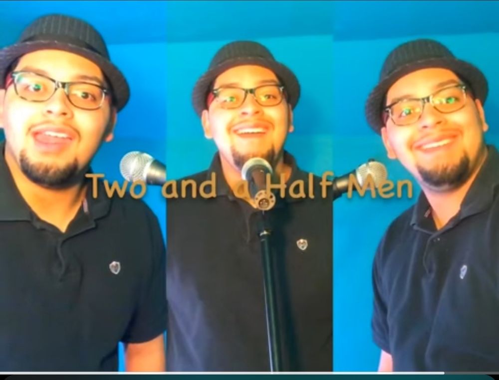 The same man three times in a black polo and pinstripe trilby hat with two and a half men in comic sans across the middle. There's also a microphone in front of the middle same man.
