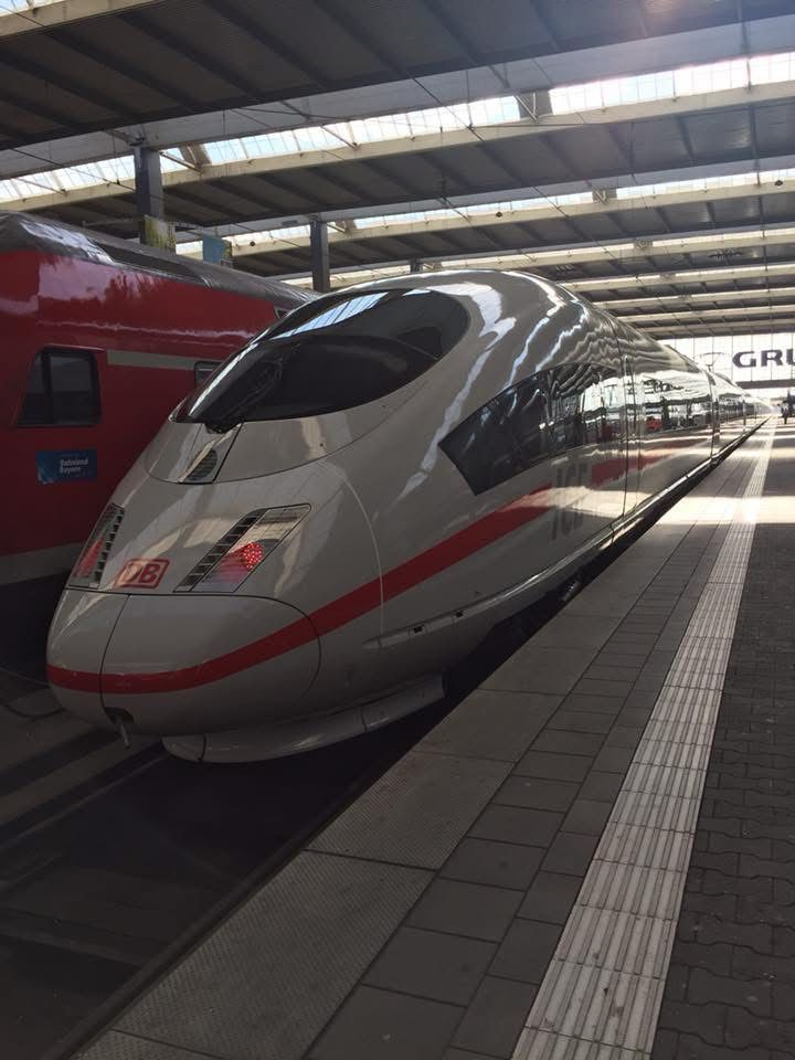 Das Bild zeigt einen glänzenden ICE-Hochgeschwindigkeitszug der Deutschen Bahn, der für moderne Hightech Qualität im deutschen Bahnverkehr steht. Der Zug mit seiner aerodynamischen Form und der charakteristischen weißen Lackierung mit rotem Streifen steht am Bahnsteig eines großen, überdachten Bahnhofs. Neben ihm befindet sich ein weiterer Zug. Die Szene vermittelt fortschrittliche Technik, Geschwindigkeit und verlässliche Mobilität.