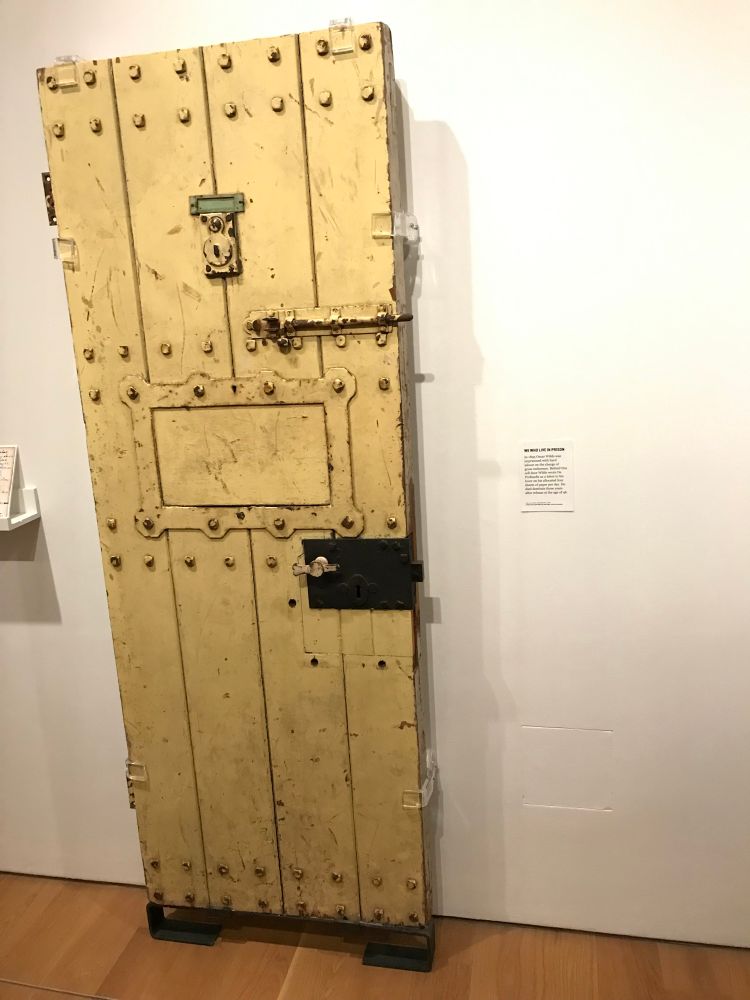 Oscar Wilde’s prison door on display at an exhibition. It is a dirty yellow, heavy door with rivets, and multiple locks and bolts.

The artist statement beside it reads, ‘In 1895 Oscar Wilde was imprisoned with hard labour on the charge of gross indecency. Behind this cell door Wilde wrote De Profundis as a letter to his lover on his allocated four sheets of paper per day. He died destitute three years after release at the age of 46.’