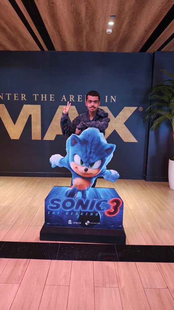 me doing the peace sign while standing behind the sonic cutout with the Sonic movie 3 logo in front of his legs