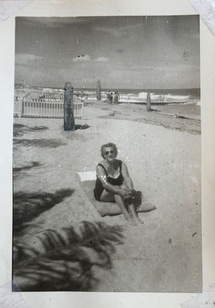 black and white photo of a woman on the beach. painted into the background are three worm like creatures with big smiles