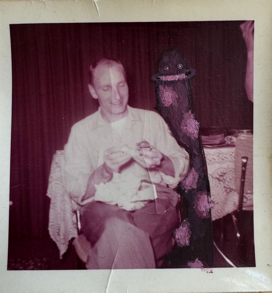 painted into an old monochromatic photograph, a worm-like creature with a large smile blends into the background behind a man sitting looking occupied with something.