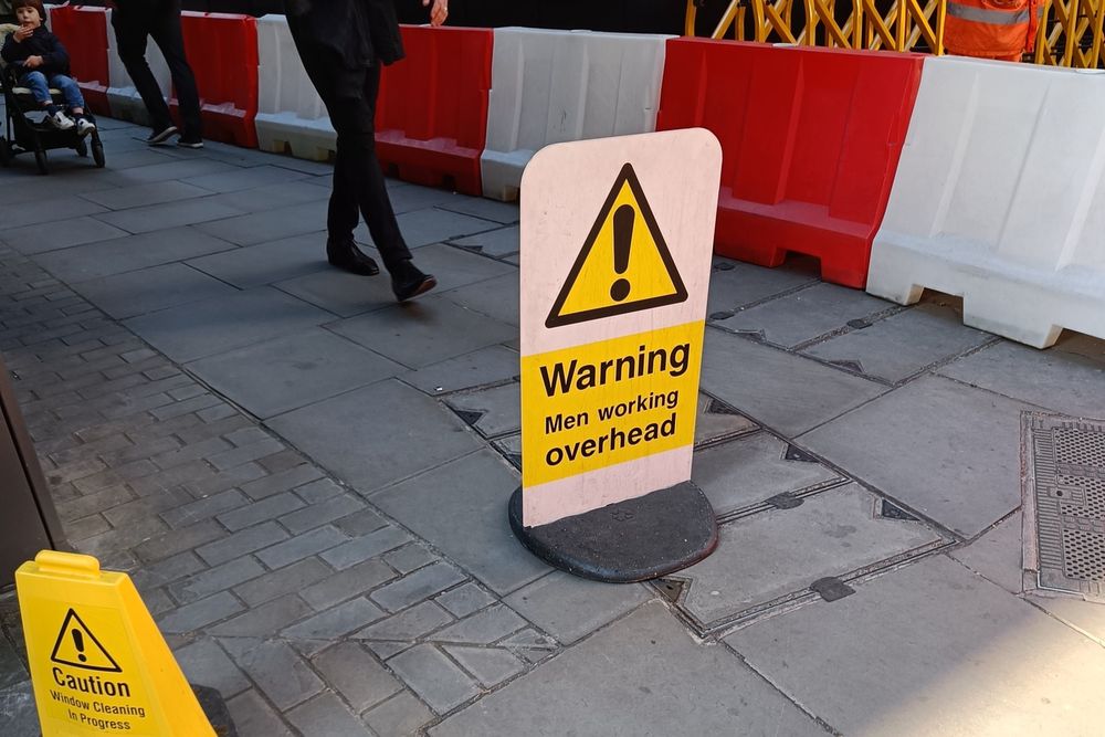 A warning sign on a street saying "⚠️Warning Men working overhead".