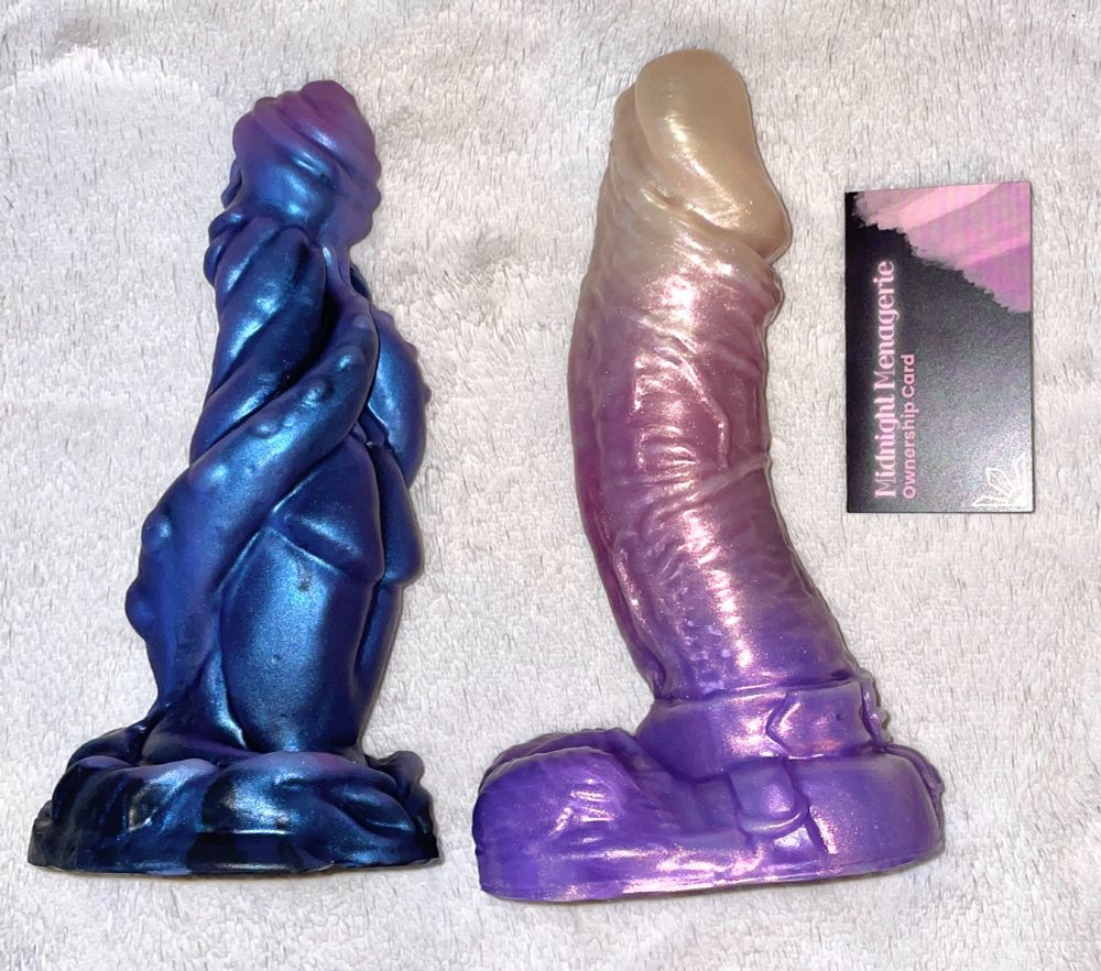 Two fantasy dildos. One is dark with blue shimmer. The other is humanoid in sunrise colors.